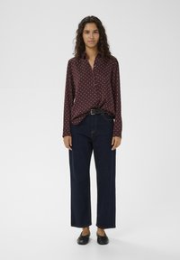 Cămașă burgundy cu nasturi și buline albe, croială lejeră, combinată cu blugi evazați de culoare închisă și pantofi negri comozi.