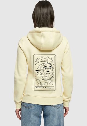 Felpa gialla con una superficie morbida, caratterizzata da un design di una carta dei tarocchi nera sul retro, che raffigura immagini del sole e della luna accompagnate dal testo "Amante del Sole & Cacciatore di Stelle".
