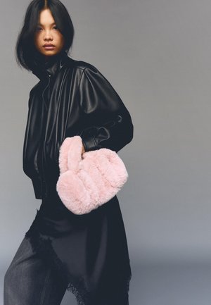 Čierna kožená bunda s vypchatými rukávmi, prehodená cez tmavý outfit, s jemnou ružovou kabelkou z umelého kožúška so zreteľne plush textúrou.