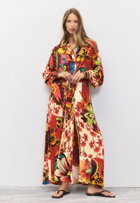 Vestito lungo a fiori con motivi audaci in rosso, giallo e verde, con colletto e bottoni sul davanti, maniche lunghe e gonna con spacco.