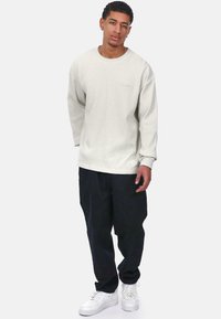 Sudadera de cuello redondo de manga larga en color beige claro con textura acanalada, combinada con pantalones negros holgados y zapatillas blancas. Diseño simple y minimalista.
