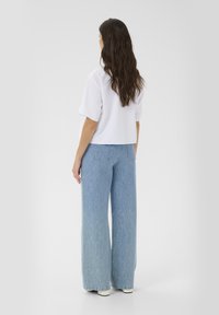 Hvid cropped t-shirt med korte ærmer parret med lyseblå vidde jeans med lodrette striber og lommer. Glat tekstur.