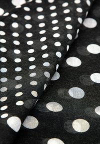 Zwarte stof met een assortiment witte stippen in verschillende groottes, met een zachte textuur en subtiele glans.