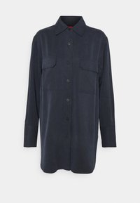 Chemise à boutons bleu marine en tissu doux, avec deux poches sur la poitrine, manches longues et col classique.