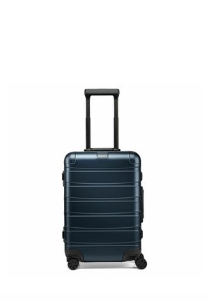 Valise rigide bleu foncé avec poignée télescopique noire déployée et quatre roulettes noires sur fond blanc.