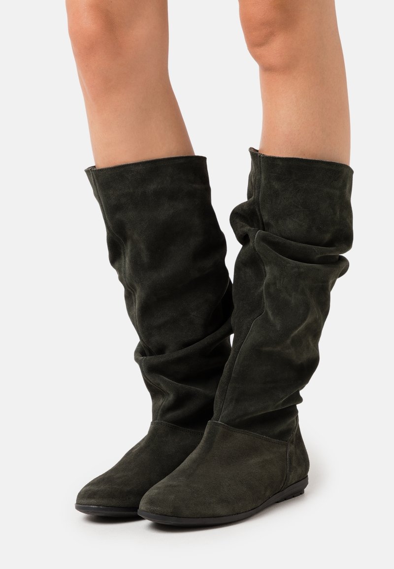 Bottes vertes en daim montant au genou, avec une texture douce, un design ample et des semelles plates. Présentent un bout arrondi et des accents minimalistes.