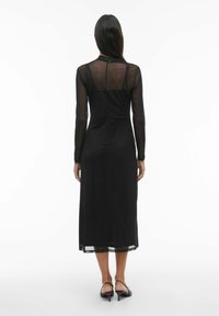 Melnas krāsas kleita ar garām caurspīdīgām piedurknēm un svārku garumu zem ceļgala. Muguras daļā caurspīdīgi paneļi, gluda tekstūra un pieguļošs siluets.