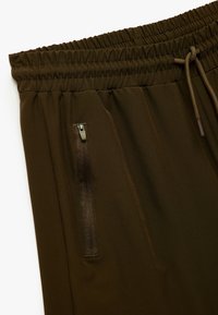Bruine sportbroeken met een elastische tailleband, trekkoord en een ritszak aan de zijkant voor veilige opslag. Glad textuur.
