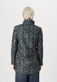 Manteau en imprimé léopard dans des tons de vert foncé et noir, doté d'un col haut et de longues manches, avec un tissu lisse et texturé.