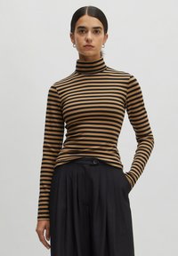 Gestreepte coltrui in bruin en zwart. Slim fit met lange mouwen, zachte textuur en een hoge kraag. Gecombineerd met zwarte geplooide broek.
