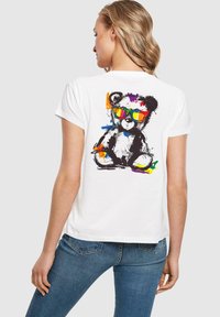 White t-shirt featuring a colorful graphic of a bear wearing sunglasses, with a textured design and splashes of bright paint.