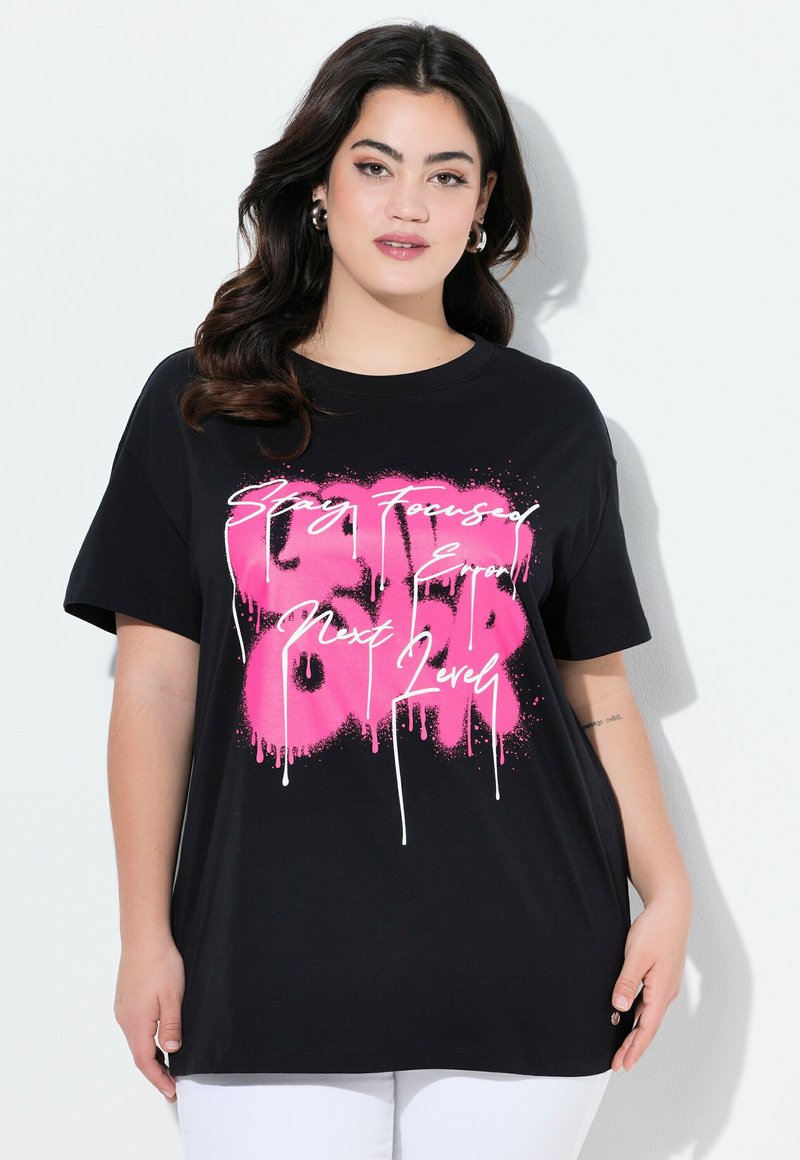 Camiseta negra oversize de algodón, con un atrevido estampado de estilo grafiti en rosa y letras blancas, mangas cortas y cuello redondo.