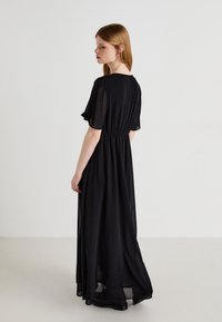 Black, long maxi dress with a flowing, lightweight fabric. Features short, ruffled sleeves and an elastic waistband for a fitted silhouette.