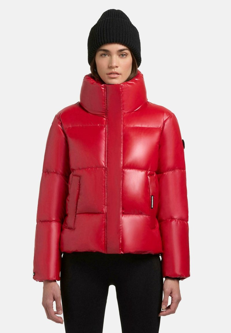 Rode pufferjack met hoge kraag, glanzende afwerking en horizontale quiltontwerpen. Heeft zijzakken en een getailleerd silhouet. Zwarte beanie gedragen.