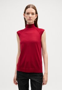 Top rosso senza maniche con collo alto e design aderente, realizzato in tessuto a maglia liscio. Presenta dettagli a coste sul collo e sull'orlo.