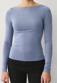 Vaaleansininen pitkähihaine paita, jossa on venepääntie, kapea muotoilu ja sileä pinta. Yhdistetty mustiin kapeisiin housuihin.