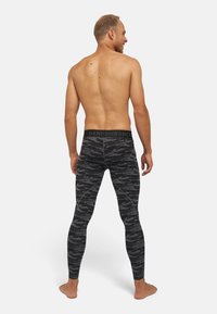 Leggings en camouflage noir avec une texture lisse, dotés d'une large ceinture de marque et d'une coupe ajustée, présentés de dos.