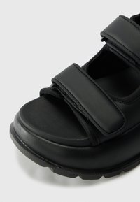 Sandalo nero con due ampie cinghie in Velcro, suola texturizzata e punta arrotondata. Realizzato in materiale sintetico con finitura opaca.