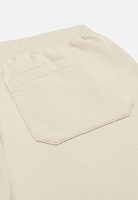 Beige sweatpants met een elastische tailleband en een enkele zak aan de achterkant, gemaakt van een zachte, textuurstof.
