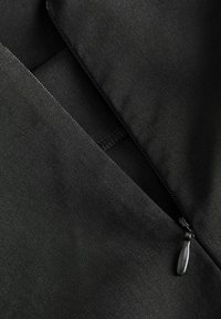 Sort stof med en glat tekstur, der har en lynlås med en sort trækstrop. Materialet er fladt og sømløst med et minimalistisk design.