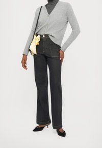 Cardigan gris côtelé avec boutons, associé à un jean en denim foncé taille haute et des chaussures à talons noires. Comprend un sac accessoire jaune à motifs.