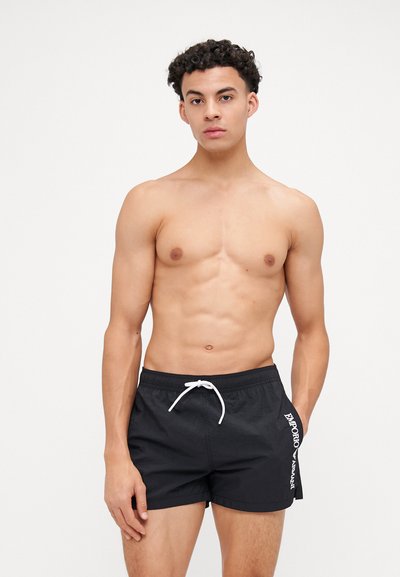 Crne kupaće kratke hlače s pojasom na čvrsto vezanje i bočnim džepovima. Sadrže bijeli natpis "Emporio Armani" sa strane. Glatki, lagani materijal.
