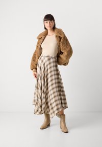 Brun faux fur jakke, beige top, rutet midi nederdel i creme, brune og grønne nuancer, og lysebrune ankelstøvler med blokhæle.
