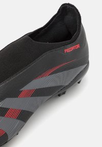 Černý fotbalový kopačka s elegantním designem, vyrobený z texturovaného syntetického materiálu, s červenými akcenty a šedými pruhy na boku.