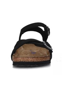 Zwarte sandal met twee banden en een verstelbare gesp, met een kurken zool en een gladde binnenzool. Schuimachtige textuur onder de banden.