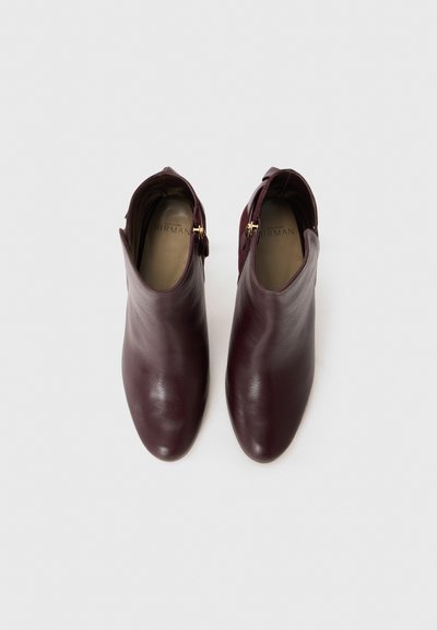 Botas tobilleras de cuero burdeos con textura suave, punta puntiaguda y cremallera lateral con detalle en tono dorado.