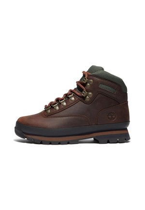 Brown leather hiking boot with black sole, metal eyelets, red and brown laces, padded green collar, and Timberland logo on heel and side.
