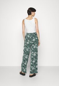 Calças impressas com flores verdes, de corte relaxado e cintura elástica, combinadas com uma blusa de alças branca e sandálias pretas.