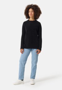 Svart långärmad tröja i ett mjukt material med rund halsringning, kombinerad med ljusblå jeans och vita sneakers. Enkel, avslappnad passform.