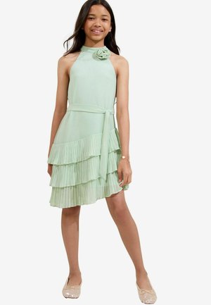 O rochie plisată de culoare verde mentă cu un guler înalt, o floare decorativă pe umăr și o curea asortată, are un design cu volane în etape.
