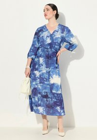 Modrá tie-dye maxi šaty s výstřihem do V, tříčtvrtečními rukávy a elastickým pasem. V kombinaci s bílou kabelkou a béžovými podpatky.