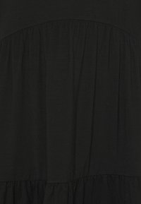 Černé šaty vyrobené z měkké tkaniny s nařaseným pasem a vrstveným spodním okrajem. Hladká textura s volným designem. Bez viditelných vzorů či akcentů.