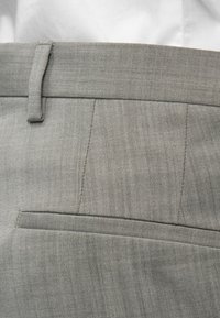 Κοντινή λήψη από τη ζώνη και την πίσω τσέπη γκρι παντελονιού, με θηλιά ζώνης, που φοριέται πάνω από ένα πουκάμισο που είναι μέσα στο παντελόνι.