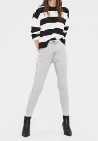 Svartvitrandig tröja med förlängda axlar, ihopparad med ljusgrå, högmidjade skinny jeans och svarta ankelstövlar.