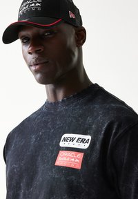 Μαύρο T-shirt με σχέδιο tie-dye και λαιμόκοψη crew, με λευκά λογότυπα "NEW ERA" και κόκκινα λογότυπα "ORACLE Red Bull RACING" στο στήθος.