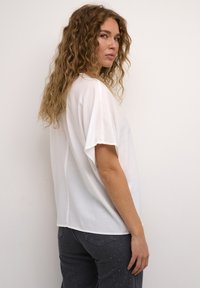 Top bianco a maniche corte con una vestibilità comoda e una texture liscia, abbinato a jeans grigio scuro con leggere decorazioni.