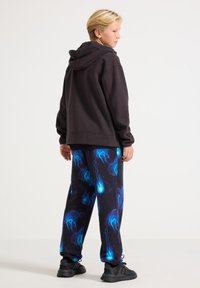 Mørkegrå hættetrøje med en afslappet pasform, kombineret med sorte joggingbukser med et levende blå vandmandemønster. Sorte sportssko fuldender looket.