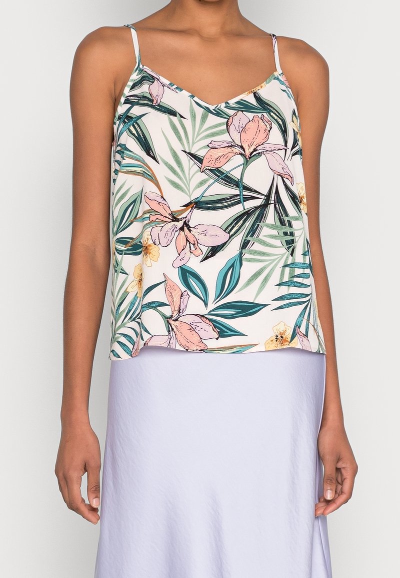 Femme portant un haut blanc sans manches avec un imprimé floral rose et vert et une jupe lavande pâle.