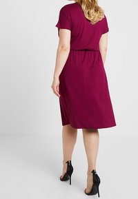 Abito a maniche corte, lunghezza al ginocchio, in tessuto bordeaux intenso. Vita elasticizzata per una vestibilità aderente, design semplice, abbinato a sandali neri con tacco alto.