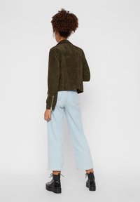 Olivgrön mockajacka i cropped modell med en slät yta, med dragkedjor vid ärmsluten, kombinerad med ljusblå vida jeans och svarta platåstövlar.