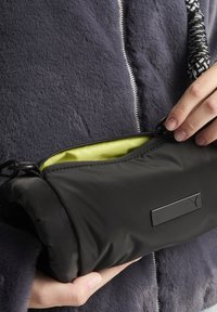 Pochette nera imbottita con una superficie liscia, dotata di chiusura a zip e interno verde brillante. Dettaglio del logo discreto all'esterno.
