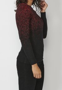 Schwarzer Pullover mit verstreuten roten Sprenkeln, Rundhalsausschnitt, langen Ärmeln, gerippten Bündchen und Saum, taillierte Form, strukturiertes Strickmaterial.