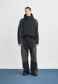 Μαύρη φούτερ με κουκούλα και υφή γκρι λεπτομέρειες, σε συνδυασμό με μαύρο και γκρι παντελόνι φαρδιάς γραμμής με ρυθμιζόμενη μέση και διακριτικά σχέδια.