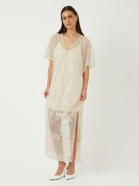 Robe maxi en dentelle blanche avec un col en V, des manches courtes à volants et un superposé transparent. Comprend des motifs floraux et des fentes latérales hautes. Texture lisse.