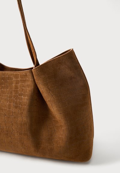 Καφέ τσάντα tote από σουέντ με υφή εμπνευσμένη από κροκόδειλο και με έναν απλό ιμάντα ώμου, εμφανίζεται σε ουδέτερο φόντο.