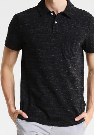 Mand iført en sort meleret kortærmet poloshirt med krave, to hvide knapper og en brystlomme.